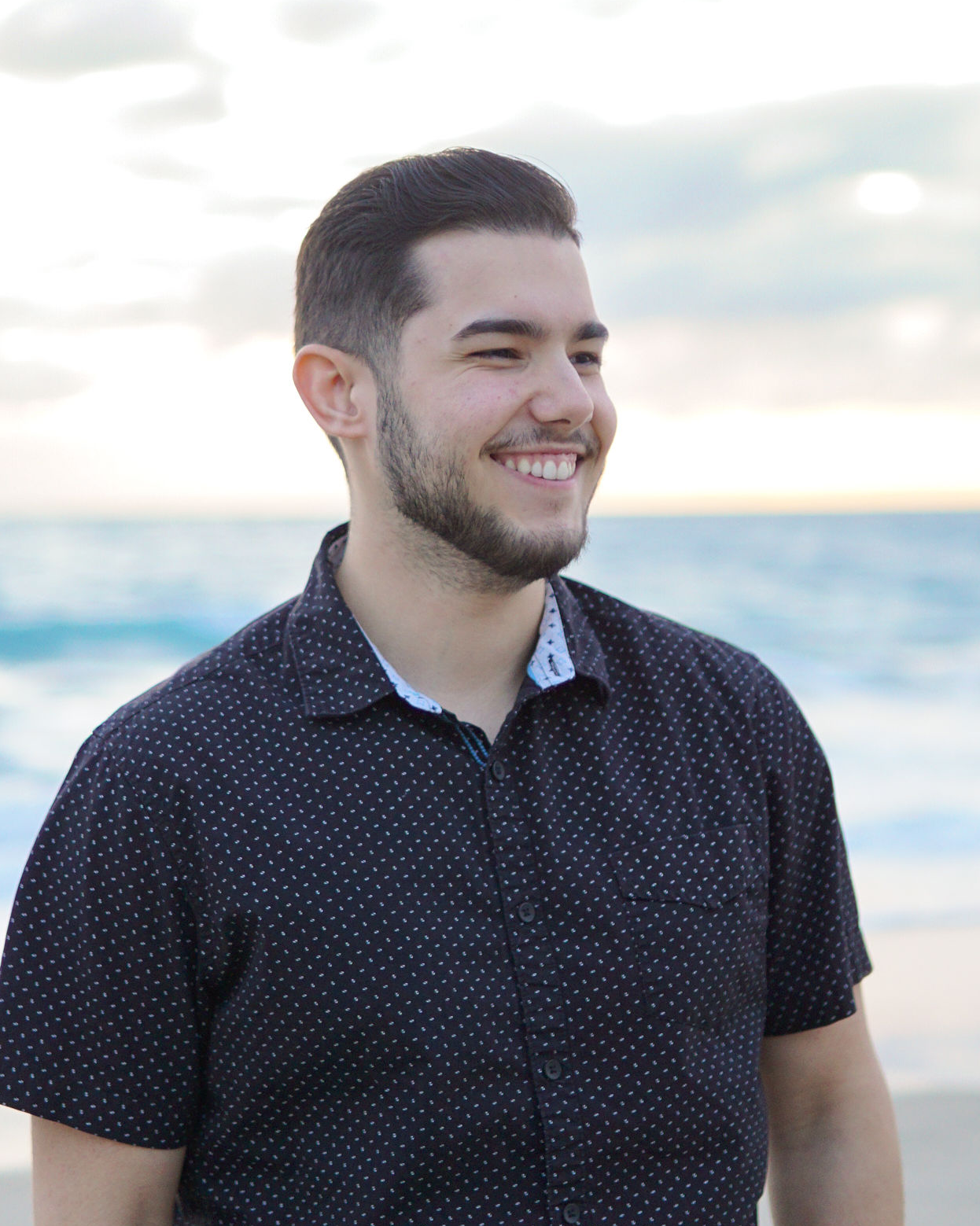 Portrait of Yerandy Orihuela Perez, owner of YopImages.com, standing by the ocean in a black patterned shirt.